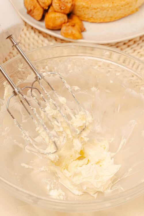 Fluffy homemade buttercream frosting being mixed in a glass bowl with an electric hand mixer.