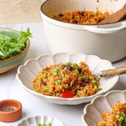 Savory vegetable fried rice in white ceramic bowls with fresh green onions and salad in the background.