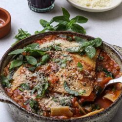 Sheet pasta with tomato sauce, fresh basil, and grated Parmesan cheese in a rustic bowl.