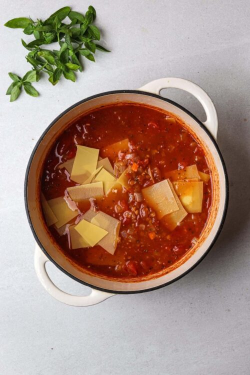 Rich tomato soup with pasta and vegetables in a white pot.