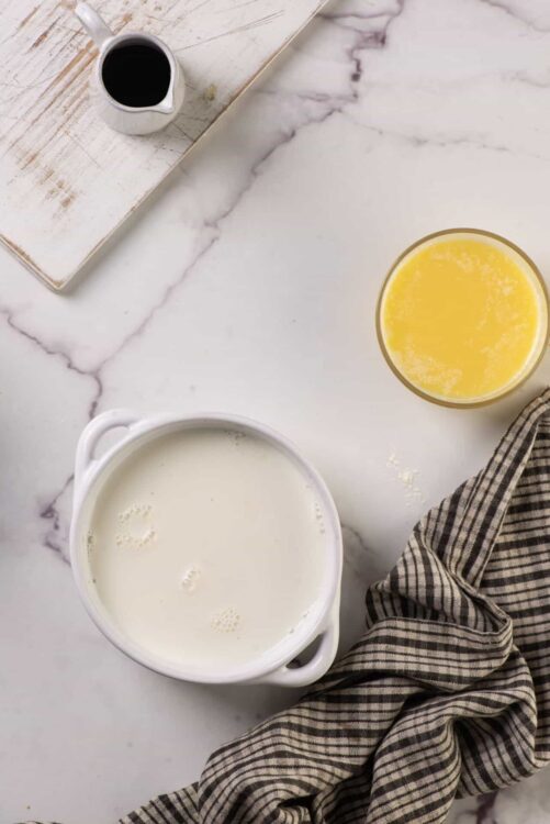 Cream, milk, and butter ingredients for baking on a marble countertop with a linen cloth.