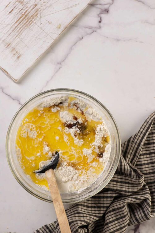 Flour, eggs, vanilla extract, and milk mixing in a glass bowl for baking.