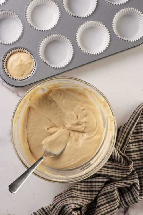 Creamy vanilla cake batter in a glass bowl with cupcake liners and a baking tray.