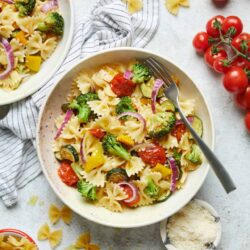 Creamy vegetable pasta salad with cherry tomatoes, broccoli, zucchini, and red onions.