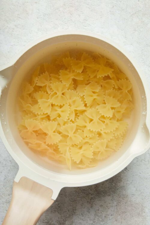 Uncooked farfalle pasta in a white pot with water.