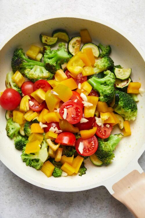 Fresh vegetable medley with broccoli, cherry tomatoes, zucchini, and yellow bell peppers in a white pan.