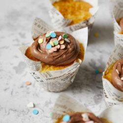Delicious cupcakes with chocolate frosting and colorful sprinkles in newspaper-style cupcake wrappers.