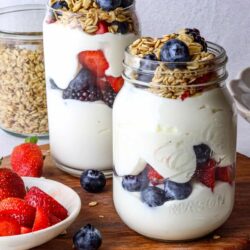 Fresh berry and yogurt parfait in mason jars with granola topping and mixed fresh berries.