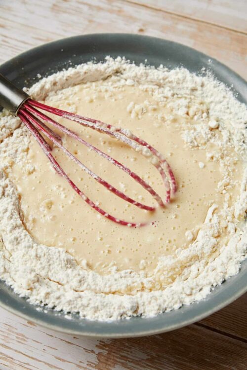 Butter crust pie dough with filling in a bowl and a pink whisk in the center.