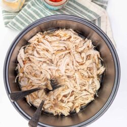 Shredded cooked chicken in a slow cooker with spices and broth.