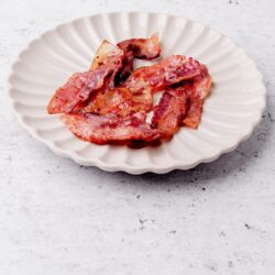 Crispy cooked bacon strips on a white scalloped plate, ready to serve.