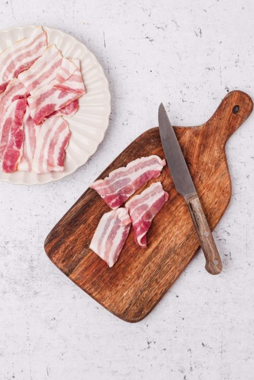 Bacon slices on a wooden cutting board and white plate, ready for cooking or breakfast.