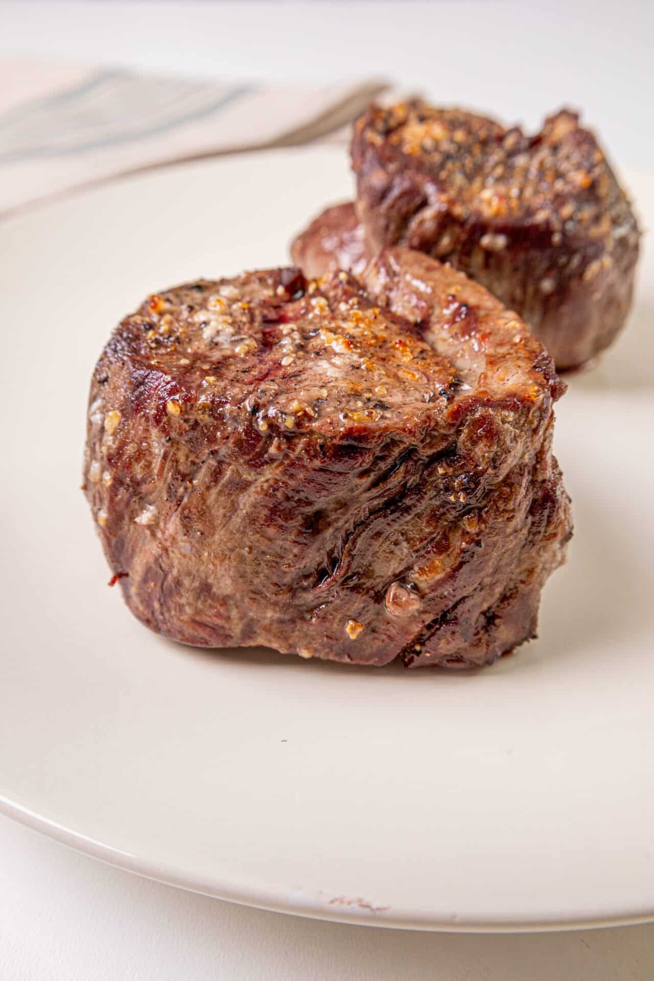 Juicy, seasoned beef tenderloin steak with a garlic and herb crust on a white plate. Perfect for special occasions and gourmet meals.