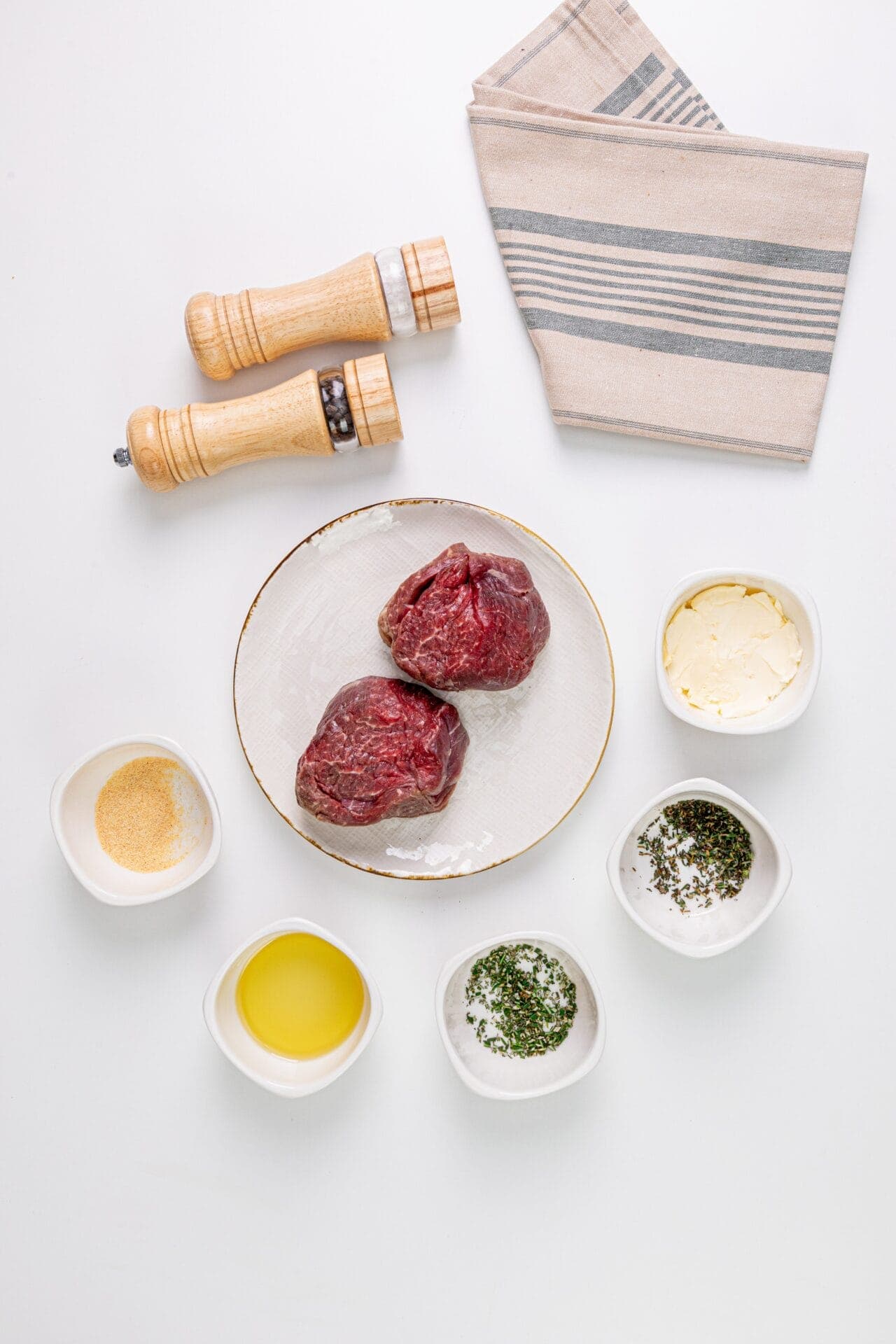 Seasoned raw beef steaks with herbs and spices on a white background.