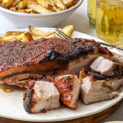 Juicy roasted pork shoulder with crispy skin served with roasted potato wedges and fresh herbs.