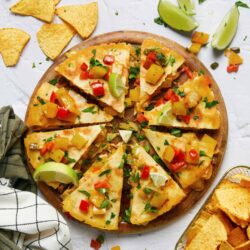 Savory veggie quesadilla with melted cheese on a wooden platter, garnished with fresh herbs and lime wedges.