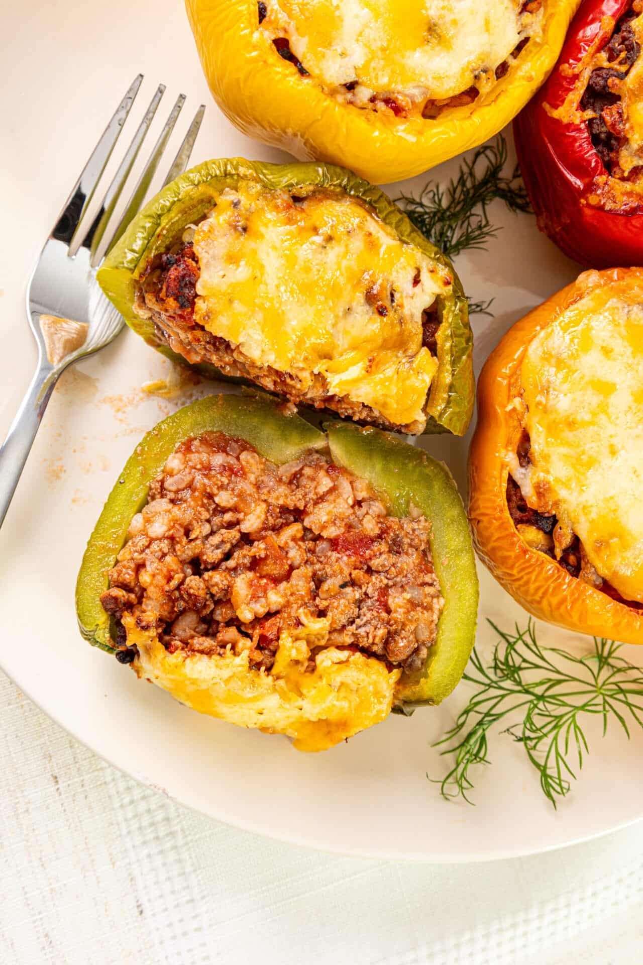 Colorful stuffed bell peppers with melted cheese and seasoned meat filling on a white plate.
