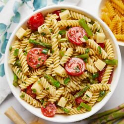 Creamy pesto pasta salad with cherry tomatoes and mozzarella cheese in a white bowl.