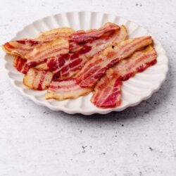 Crispy bacon strips on a white scalloped plate for breakfast or cooking ideas.