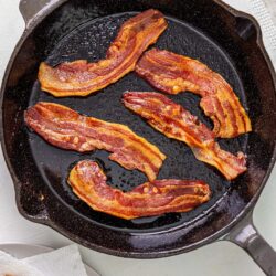 Crispy bacon strips cooking in a cast iron skillet for breakfast or brunch.