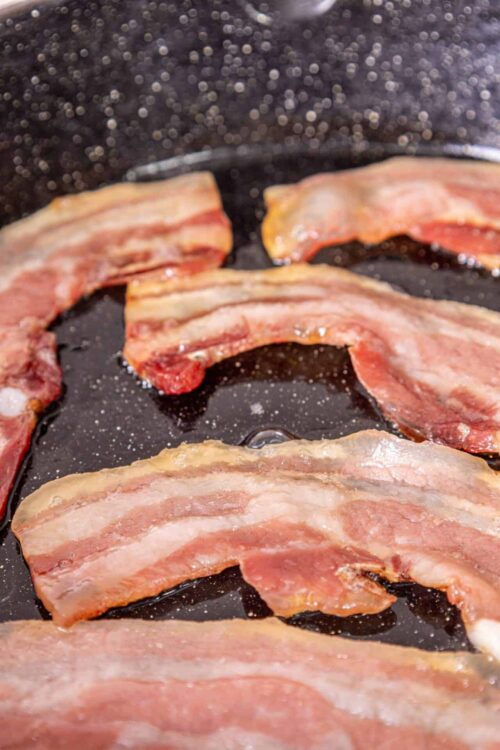 Crispy bacon cooking in a black skillet, perfect for breakfast or adding flavor to dishes.