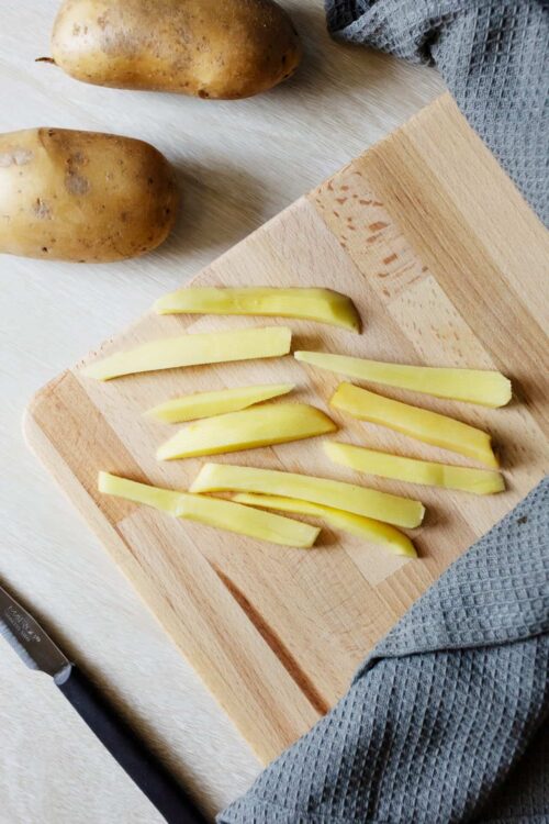 Sliced yellow potatoes on wooden cutting board for baking or roasting.