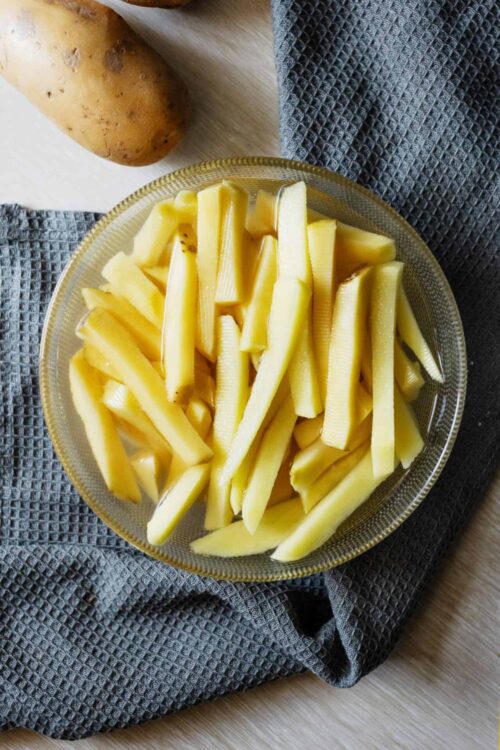 Baked potato fries in a glass bowl on a gray napkin.