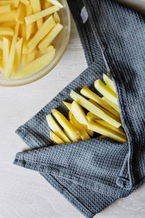 Golden baked potato fries in a gray textured towel, ready to serve.