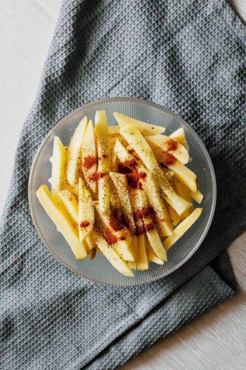 Crispy oven-baked potato fries seasoned with paprika and black pepper, served on a glass plate.