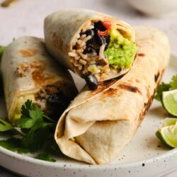 Crispy black bean and rice burrito with avocado and fresh herbs plated on a white dish.