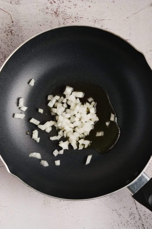 Diced onions sautéing in a black frying pan for cooking recipes.