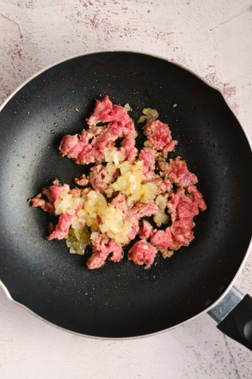 Cooking ground beef and onions in a black skillet for a recipe.
