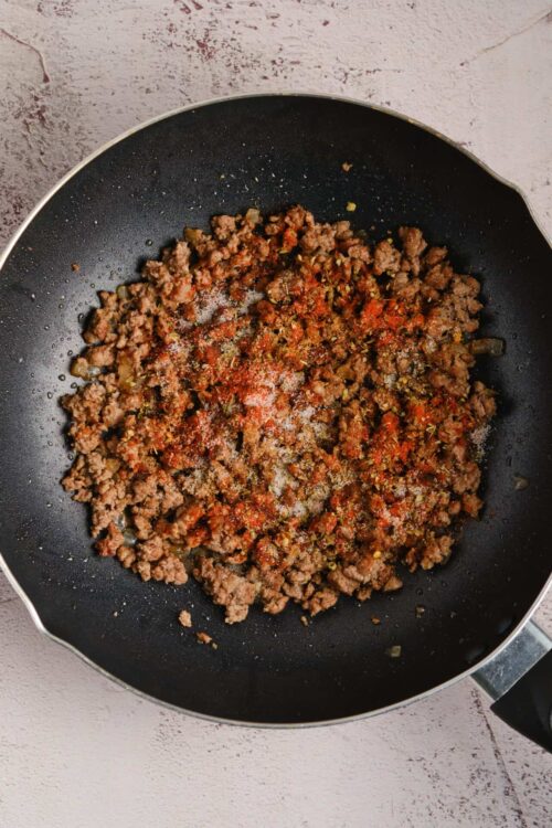 Savory ground beef cooking in a black frying pan, seasoned with spices and herbs.