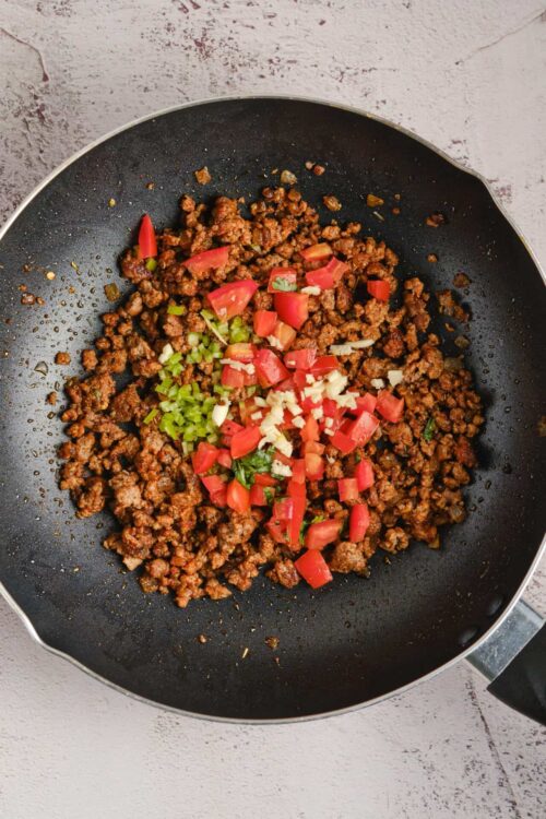 Savory cooked ground beef with diced tomatoes, green onions, and garlic in a black skillet.
