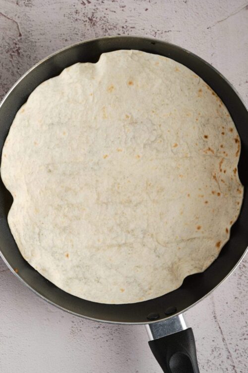 Cream cheese tortilla for baked Brie appetizer on a non-stick skillet.