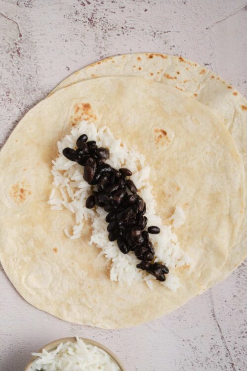 Fresh flour tortillas with shredded cheese and black beans, ready for a homemade taco.