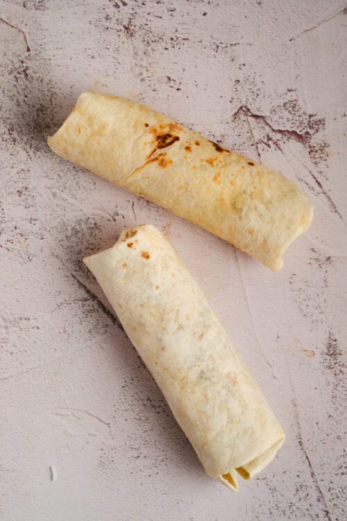 Golden baked burritos with crispy tortillas on a textured light pink background.