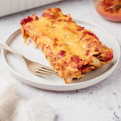 Creamy baked spaghetti casserole with melted cheese on white plate.