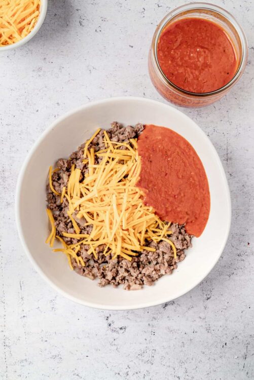 Ground beef, shredded cheddar cheese, and tomato sauce in a white bowl for Nachos.
