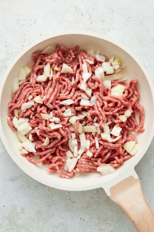 Ground beef with chopped onions in a white skillet, ready for cooking.