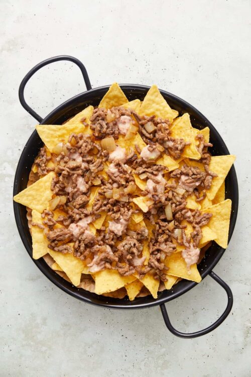 Crispy tortilla chips with seasoned ground beef and melted cheese in a black skillet.