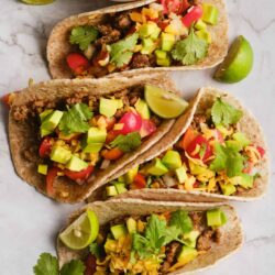 Savory tacos with ground beef, fresh tomatoes, avocado, shredded cheese, and cilantro on whole wheat tortillas.