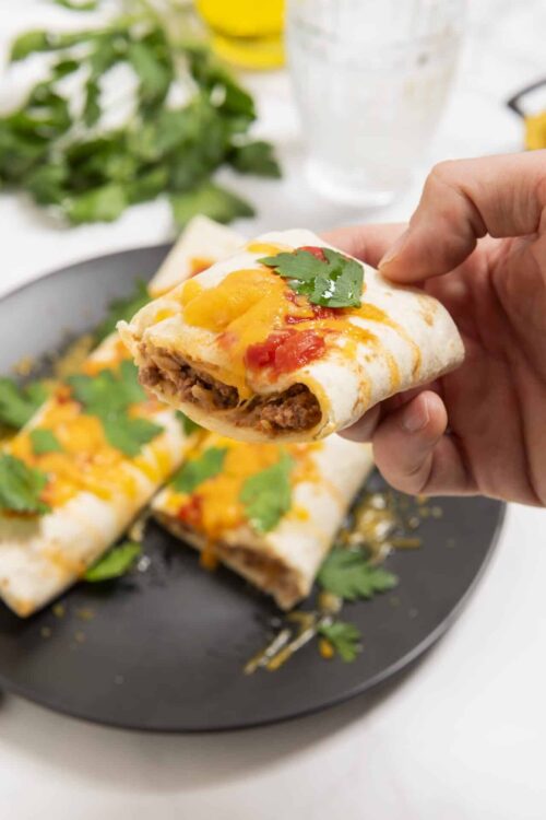 Savory beef and cheese quesadilla with melted cheese, fresh herbs, and tomato sauce on a black plate.