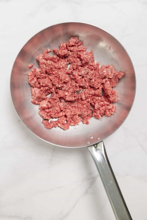 Crumbled raw ground beef in a stainless steel skillet.