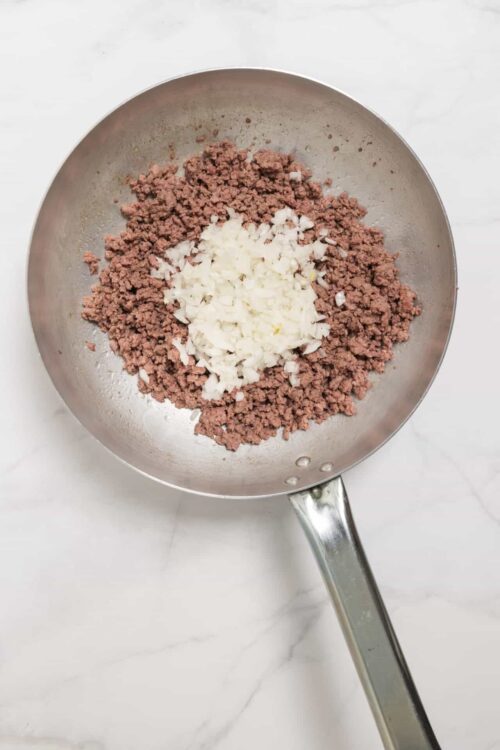 Ground beef and diced onions cooking in a stainless steel skillet for a meat filling.