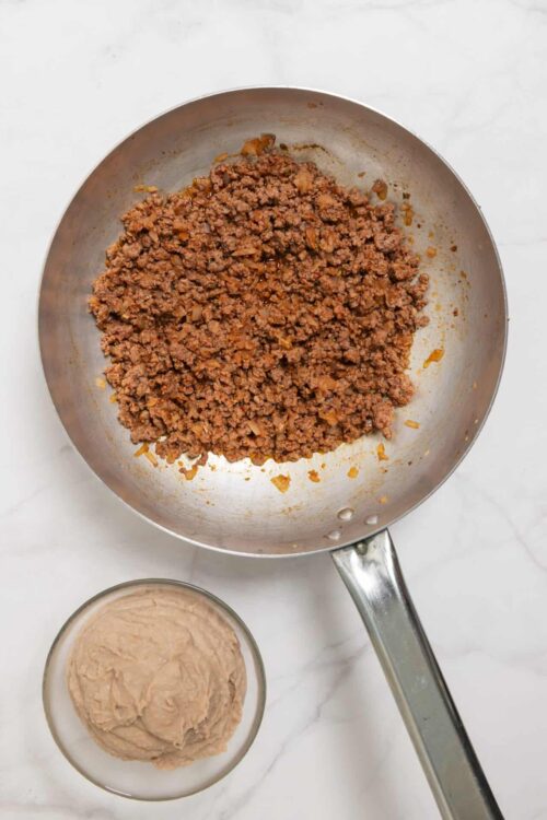 Seasoned ground beef in a stainless steel skillet with a bowl of mashed sweet potatoes nearby.