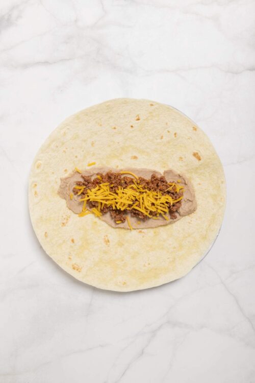 Shredded cheddar cheese beef taco filling on soft flour tortilla for homemade tacos.