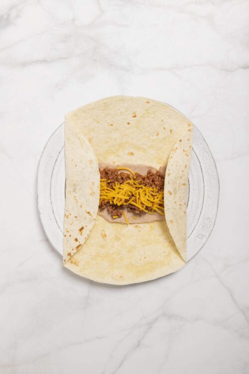Ground beef taco with shredded cheese in soft flour tortilla, on marble surface.