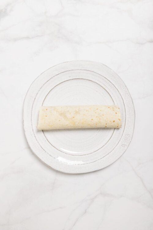 Unrolled flour tortilla on white plate for homemade burritos or wraps.