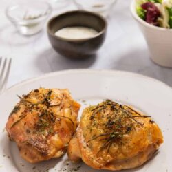 Succulent roasted chicken thighs garnished with herbs on a white plate.